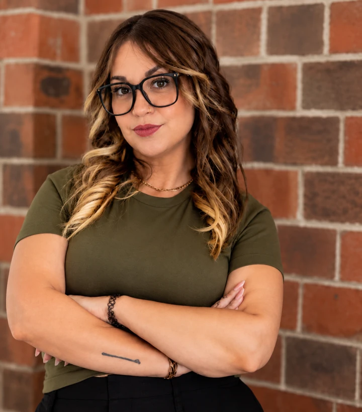 Danielle Penz standing with arms crossed in front of a brick wall